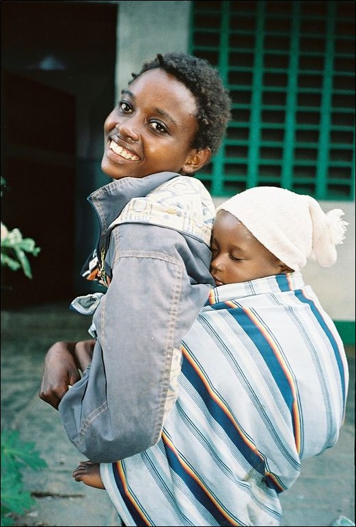 A young African woman carrying child in a baby sling.